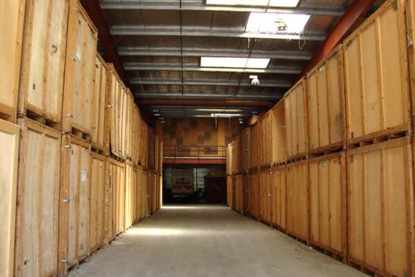 Une allée d’entrepôt bordée de caisses de garde-meubles en bois, empilées sur deux niveaux