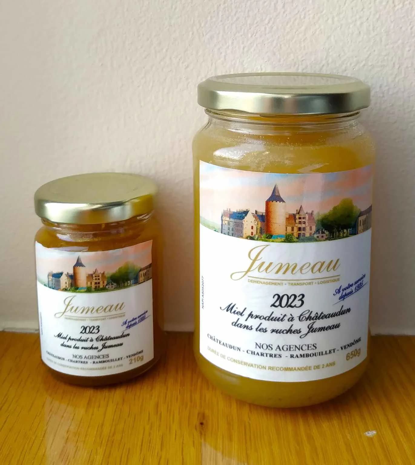 Deux pots de miel étiquetés « Miel produit à Châteaudun dans les ruches Jumeau », sur un plan de bois