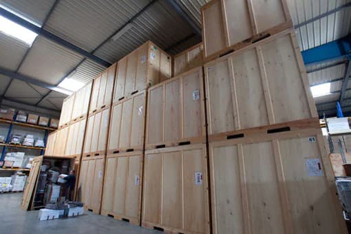 Des caisses de garde-meubles en bois empilées dans un entrepôt, une personne range un carton dans l’une d’elles