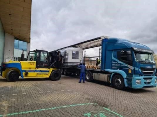 Un chariot élévateur jaune décharge une machine emballée d’un camion bâché des Transports Jumeau