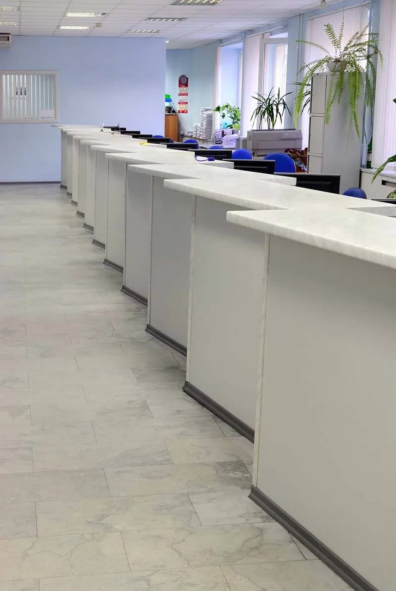 Une longue rangée de guichets dans un bureau clair, écrans et fauteuils bleus derrière le comptoir