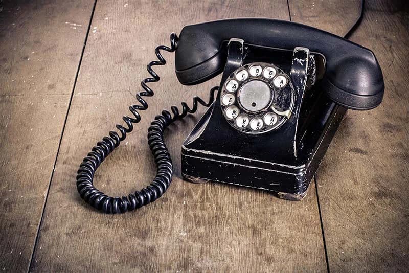 Un ancien téléphone noir à cadran, posé sur un plancher de bois