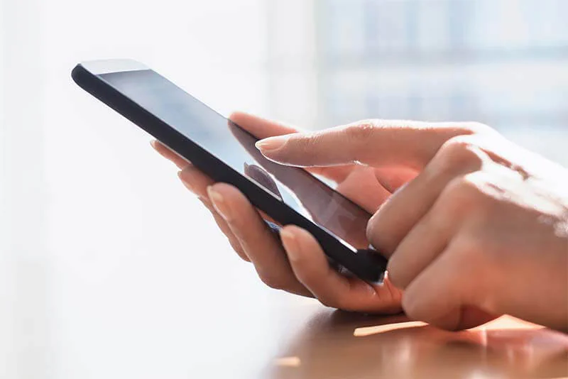 Des mains tiennent un smartphone, un doigt posé sur l’écran