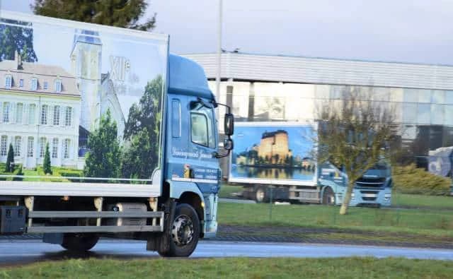 Deux camions aux caisses décorées de châteaux, sur une route devant un bâtiment d’activité
