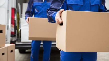 Deux déménageurs en tenue bleue portent des cartons à la sortie d’un fourgon