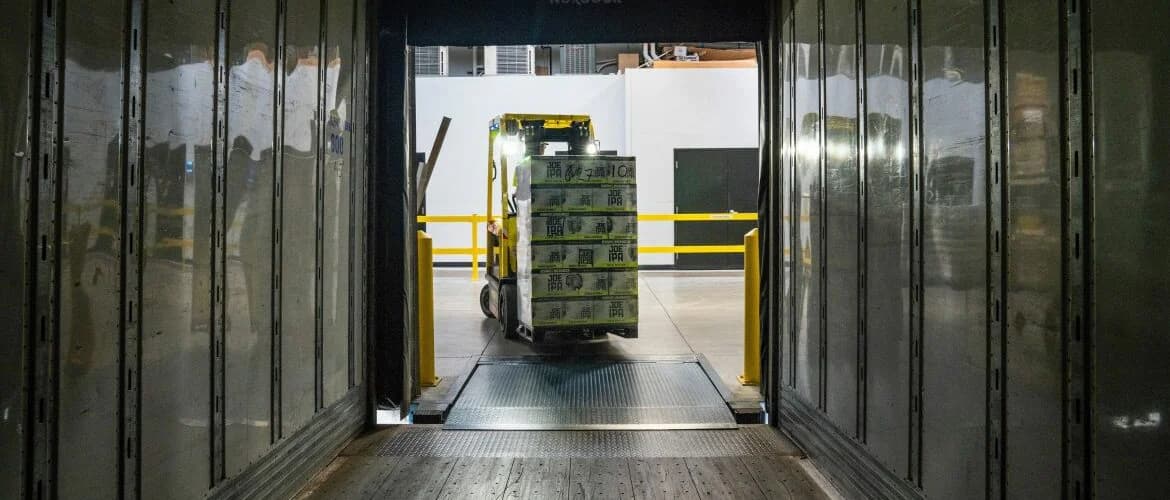 Depuis l’intérieur d’une remorque à quai, un chariot élévateur apporte une palette chargée de cartons
