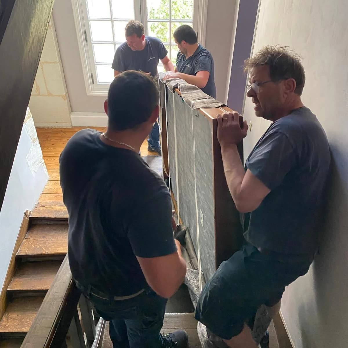 Quatre déménageurs montent un billard emballé dans un escalier