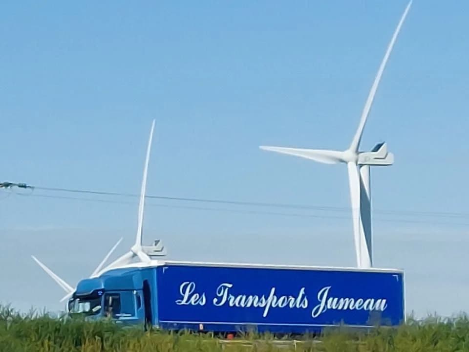 Un camion des Transports Jumeau longe un champ, devant deux éoliennes