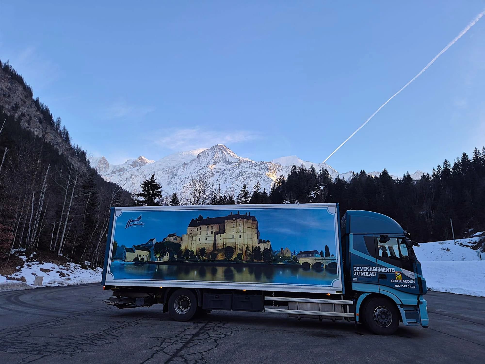 Un camion des Déménagements Jumeau sur un parking enneigé, au pied des montagnes, en Italie