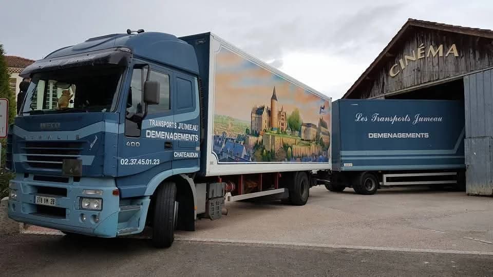 Un camion des Transports Jumeau de Châteaudun, habillé d’une peinture de château, devant un bâtiment marqué « Cinéma »