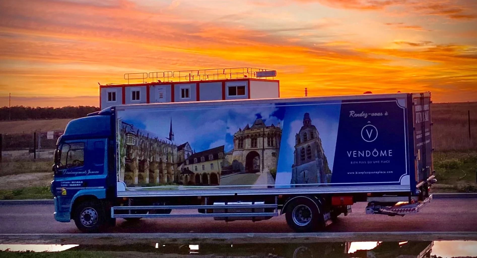 Un camion des Déménagements Jumeau habillé d’une affiche « Rendez-vous à Vendôme », sous un ciel de soleil couchant