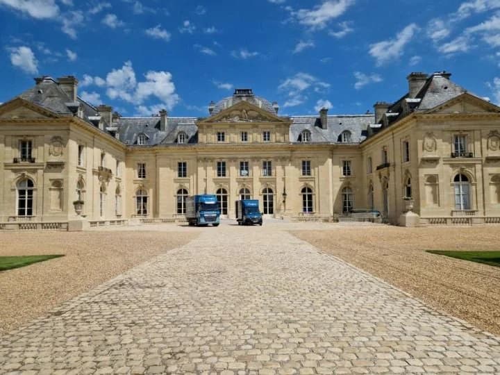 Deux camions bleus de Jumeau garés au fond de la cour pavée d’un grand château