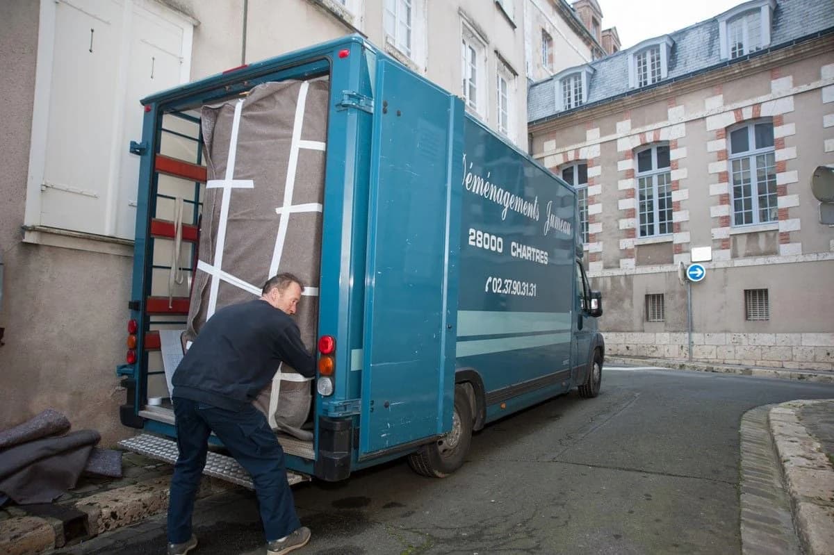 Un déménageur charge un meuble emballé dans un camion des Déménagements Jumeau de Chartres, au pied d’un immeuble ancien