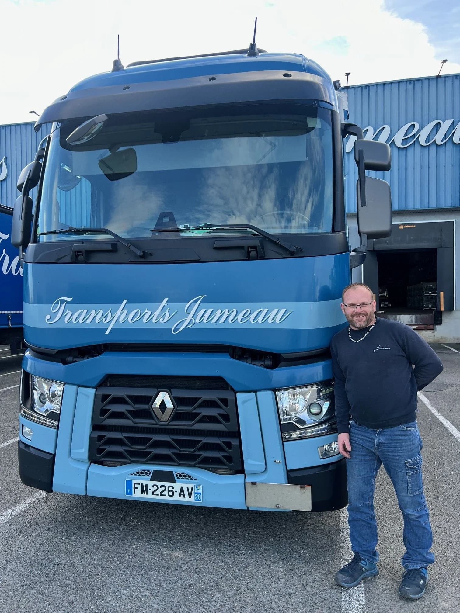 Un chauffeur à côté de son camion des Transports Jumeau, devant un bâtiment de l’entreprise