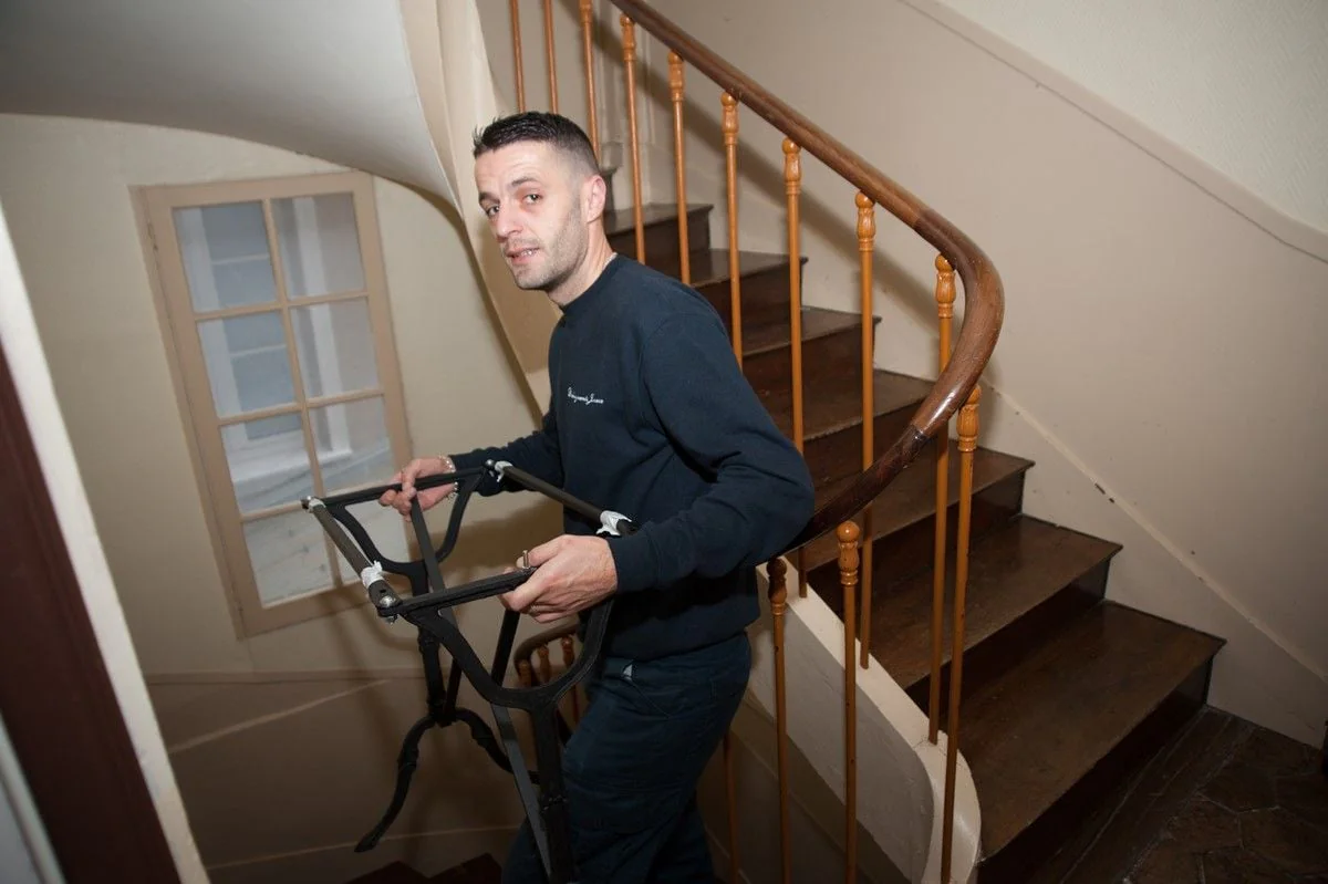 Un déménageur porte un meuble en fer forgé dans un escalier tournant