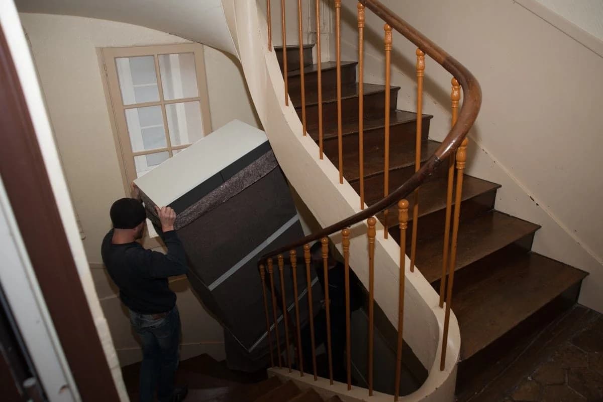 Un déménageur monte un meuble emballé dans un escalier tournant