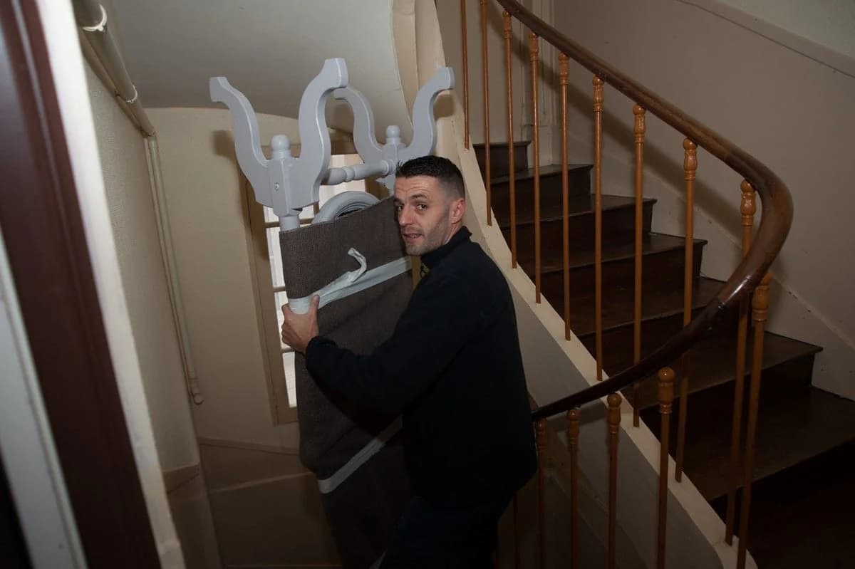 Un déménageur descend un escalier tournant avec un meuble emballé aux pieds sculptés