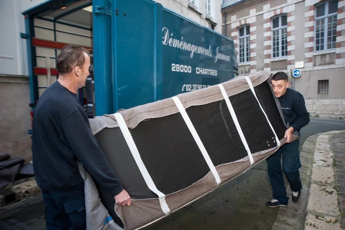 Deux déménageurs portent un canapé emballé vers un camion des Déménagements Jumeau de Chartres