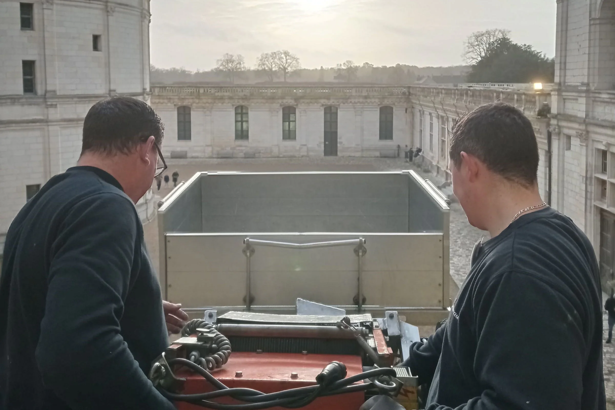 Deux déménageurs règlent un monte-charge au-dessus de la cour d’un château
