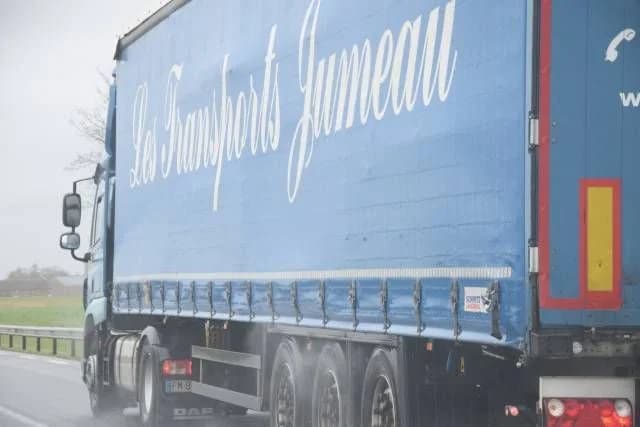Une semi-remorque bâchée des Transports Jumeau sur une route mouillée