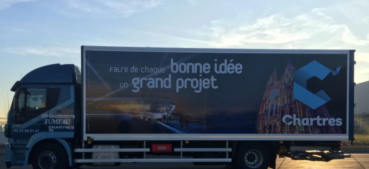 Un camion des Déménagements Jumeau, la caisse habillée d’un visuel de Chartres : une cathédrale illuminée et les mots « faire de chaque bonne idée un grand projet »