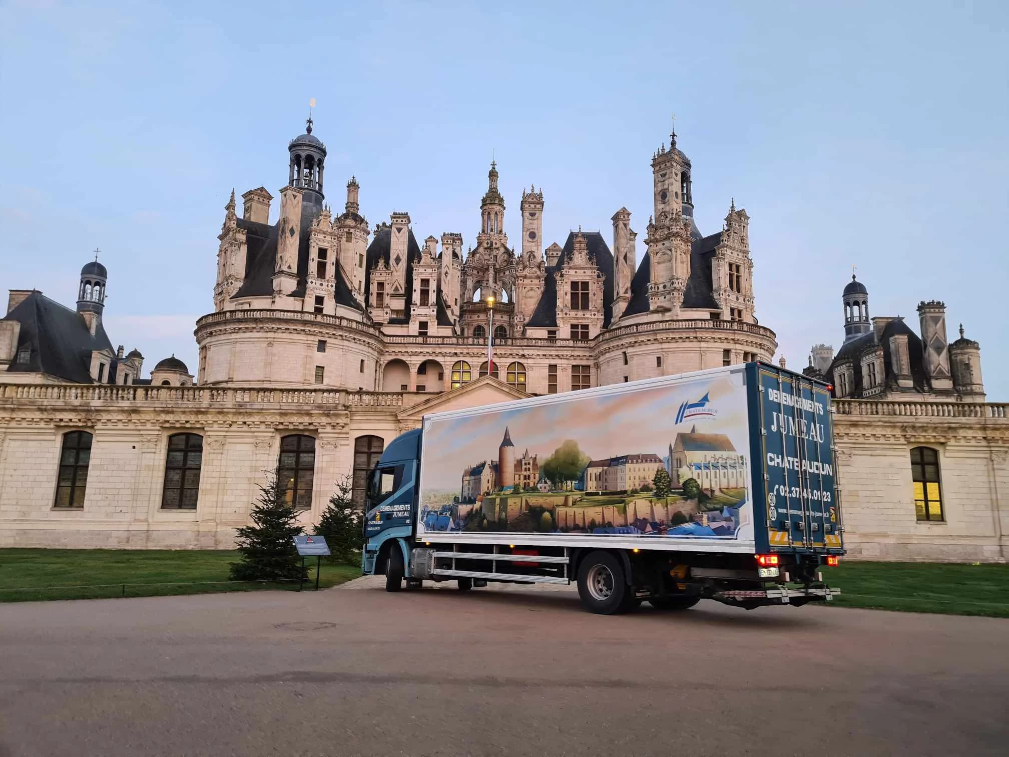 Un camion des Déménagements Jumeau, à la caisse peinte d’une vue de Châteaudun, devant le château de Chambord