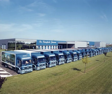 Une longue file de camions bleus garés devant un bâtiment à l’enseigne des Transports Jumeau