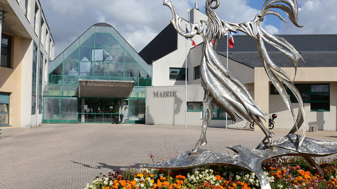 La mairie de Saran, son entrée vitrée et, au premier plan, une sculpture d’acier au-dessus d’un massif fleuri