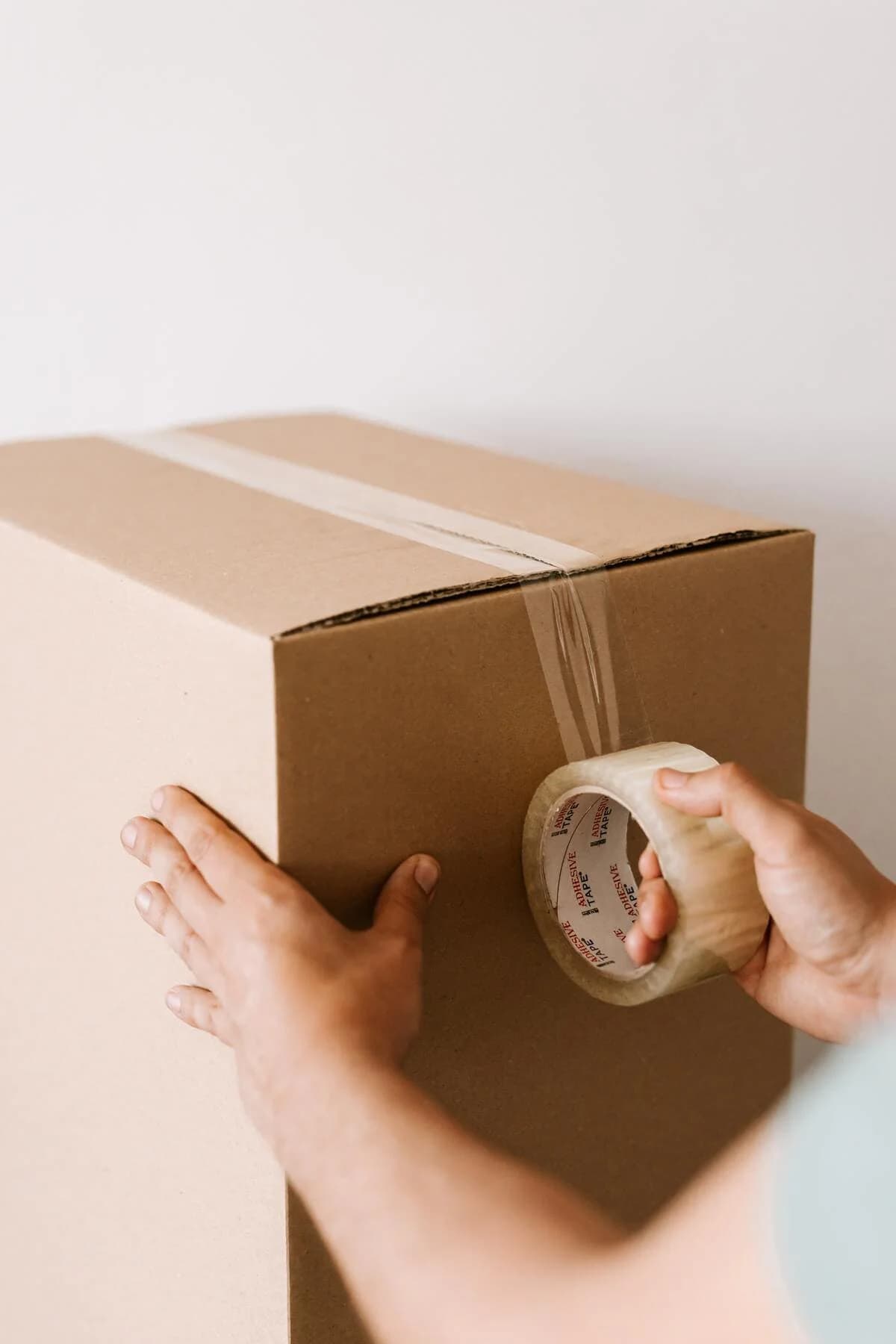 Des mains ferment un carton de déménagement avec un rouleau de ruban adhésif