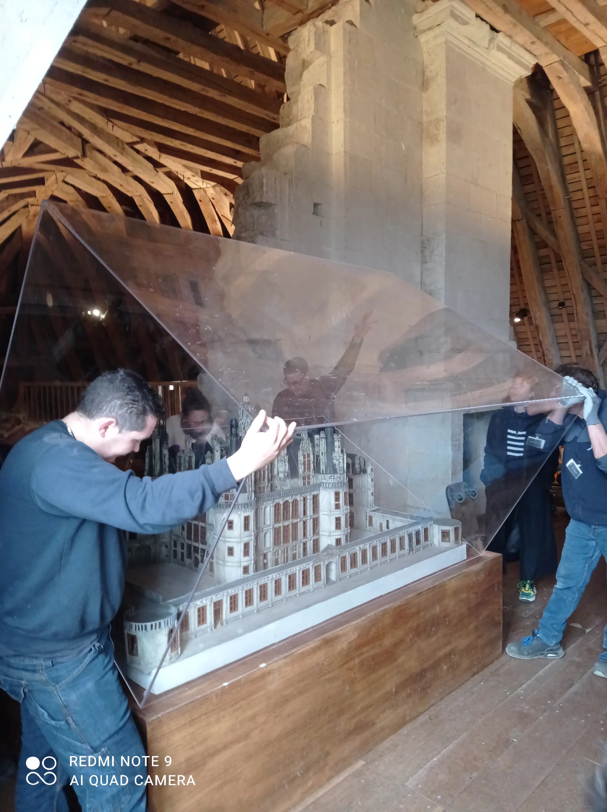 Des déménageurs Jumeau soulèvent la cloche transparente qui protège la maquette d’un château