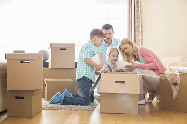 Des parents et leurs deux enfants autour d’un carton ouvert, dans un salon encombré de cartons