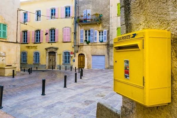 Une boîte aux lettres jaune de La Poste, fixée à un mur au coin d’une petite place pavée