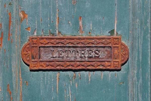 Une plaque de boîte aux lettres en fonte rouillée, marquée « Lettres », sur une vieille porte verte écaillée