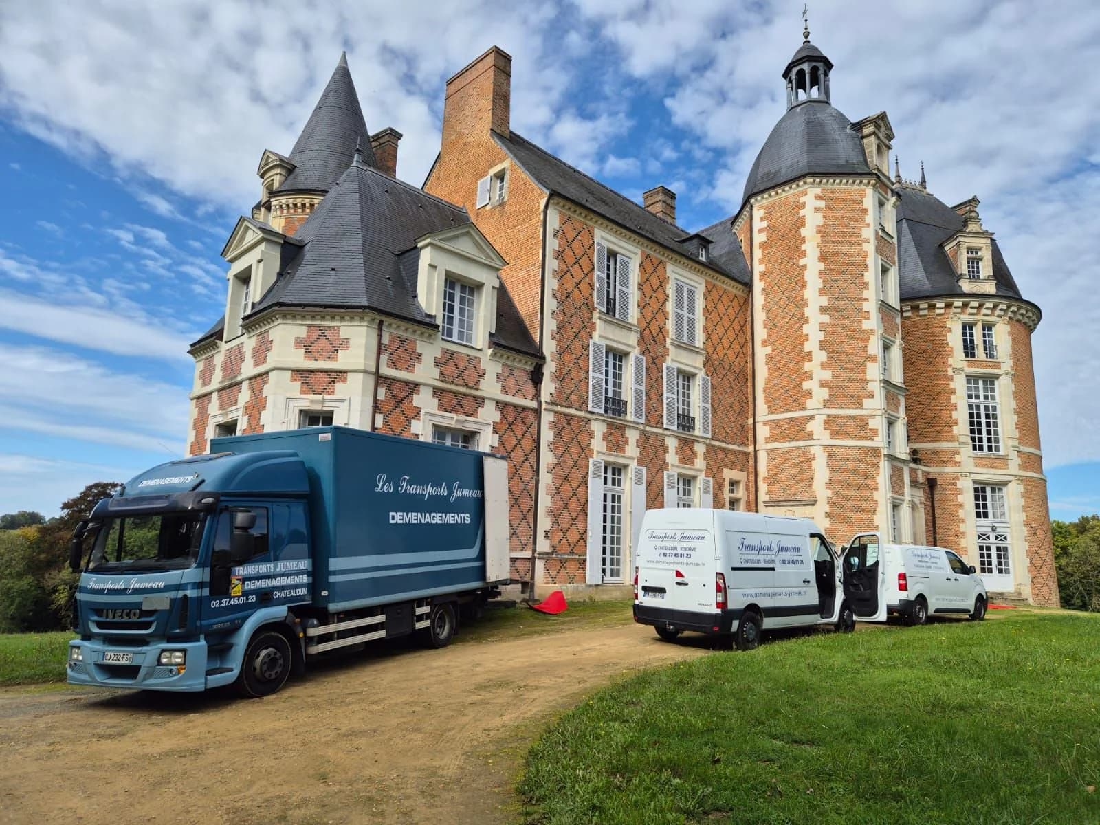Un camion et deux fourgons de Jumeau devant un château de brique à tourelles