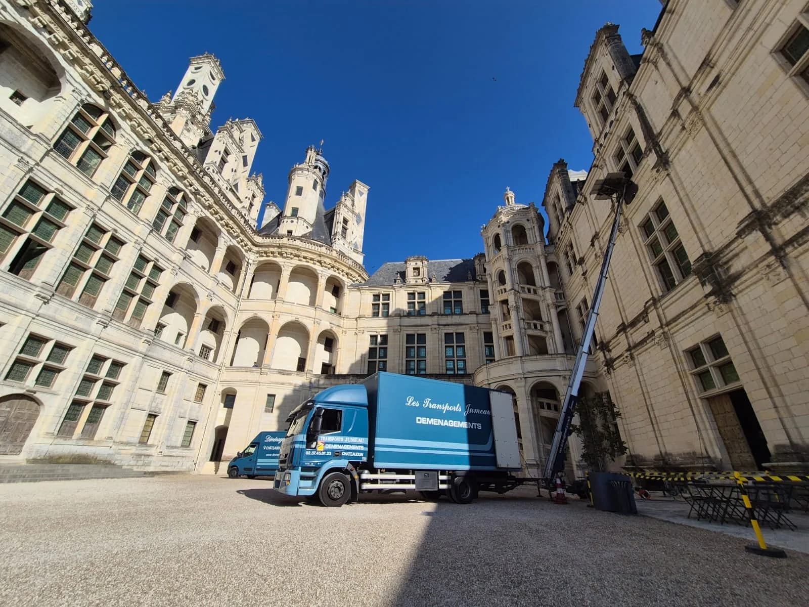Un camion des Transports Jumeau dans la cour d’un château, un monte-meubles dressé le long de la façade