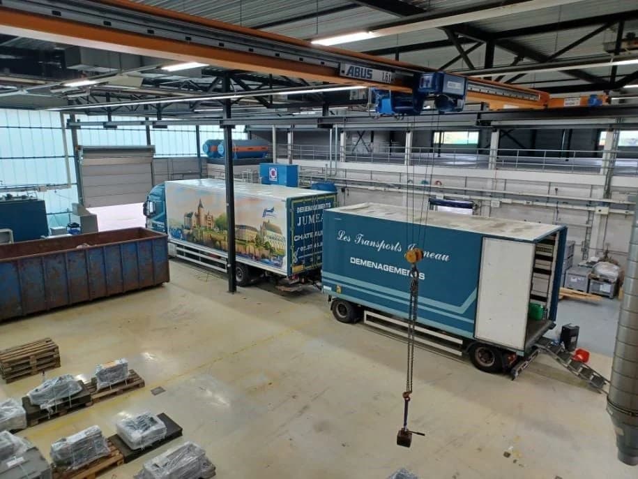 Deux camions de Jumeau, dont un des Transports Jumeau, à l’intérieur d’un grand atelier