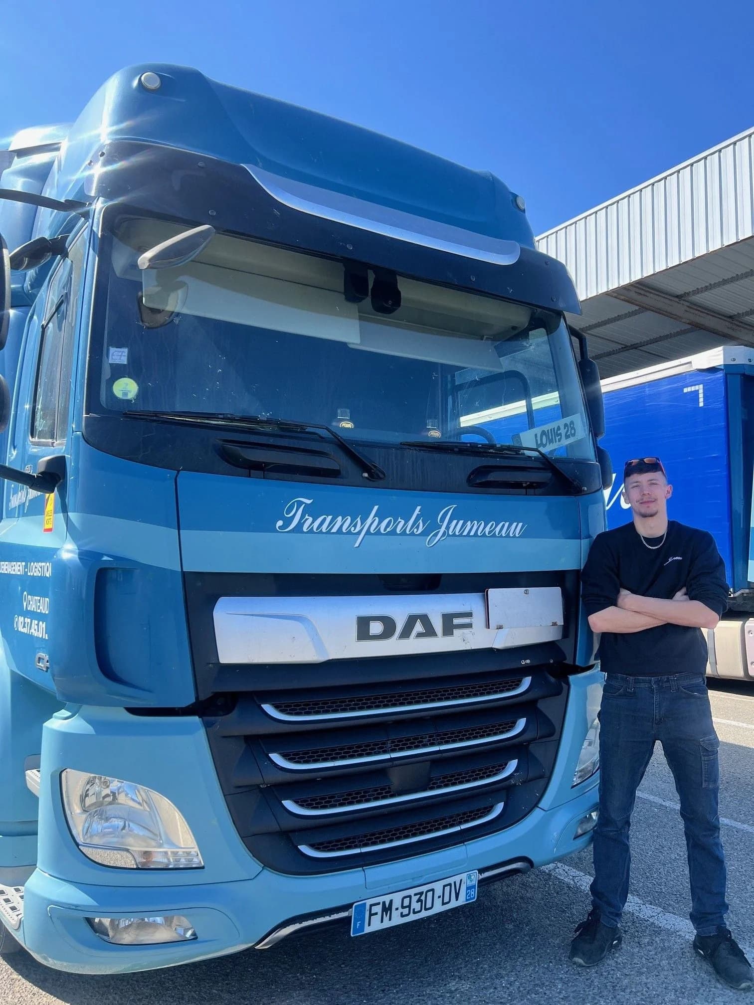 Un jeune chauffeur, bras croisés, à côté d’un camion DAF des Transports Jumeau