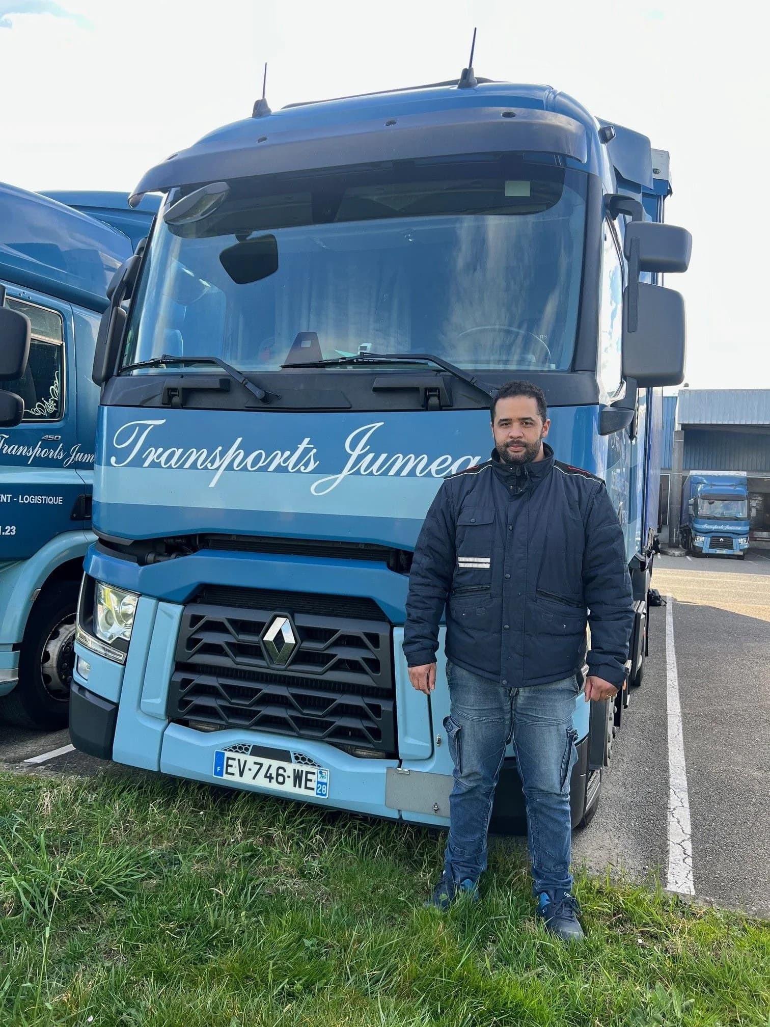 Un chauffeur devant un camion bleu des Transports Jumeau, garé au bord d’une pelouse