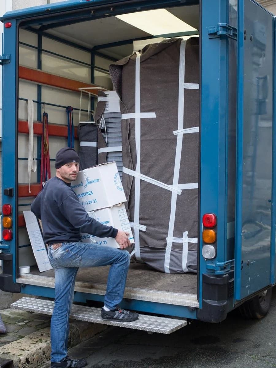 Un déménageur monte des cartons dans un camion, à côté d’un meuble emballé