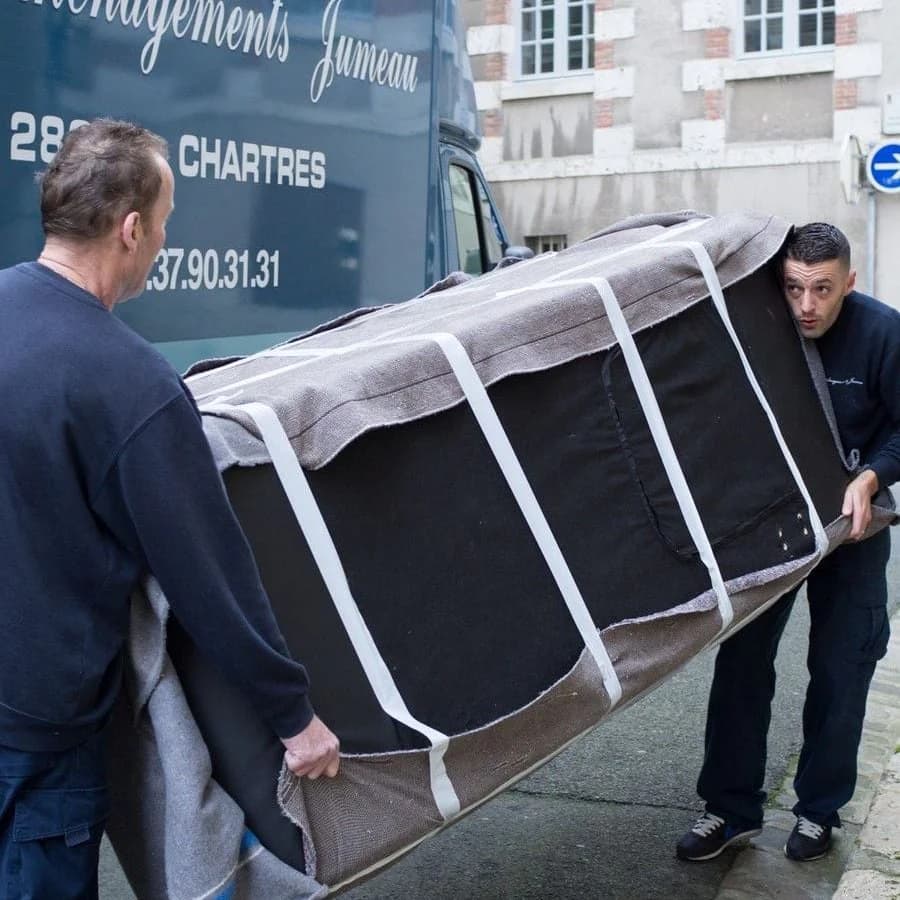 Deux déménageurs portent un meuble emballé devant un camion des Déménagements Jumeau de Chartres
