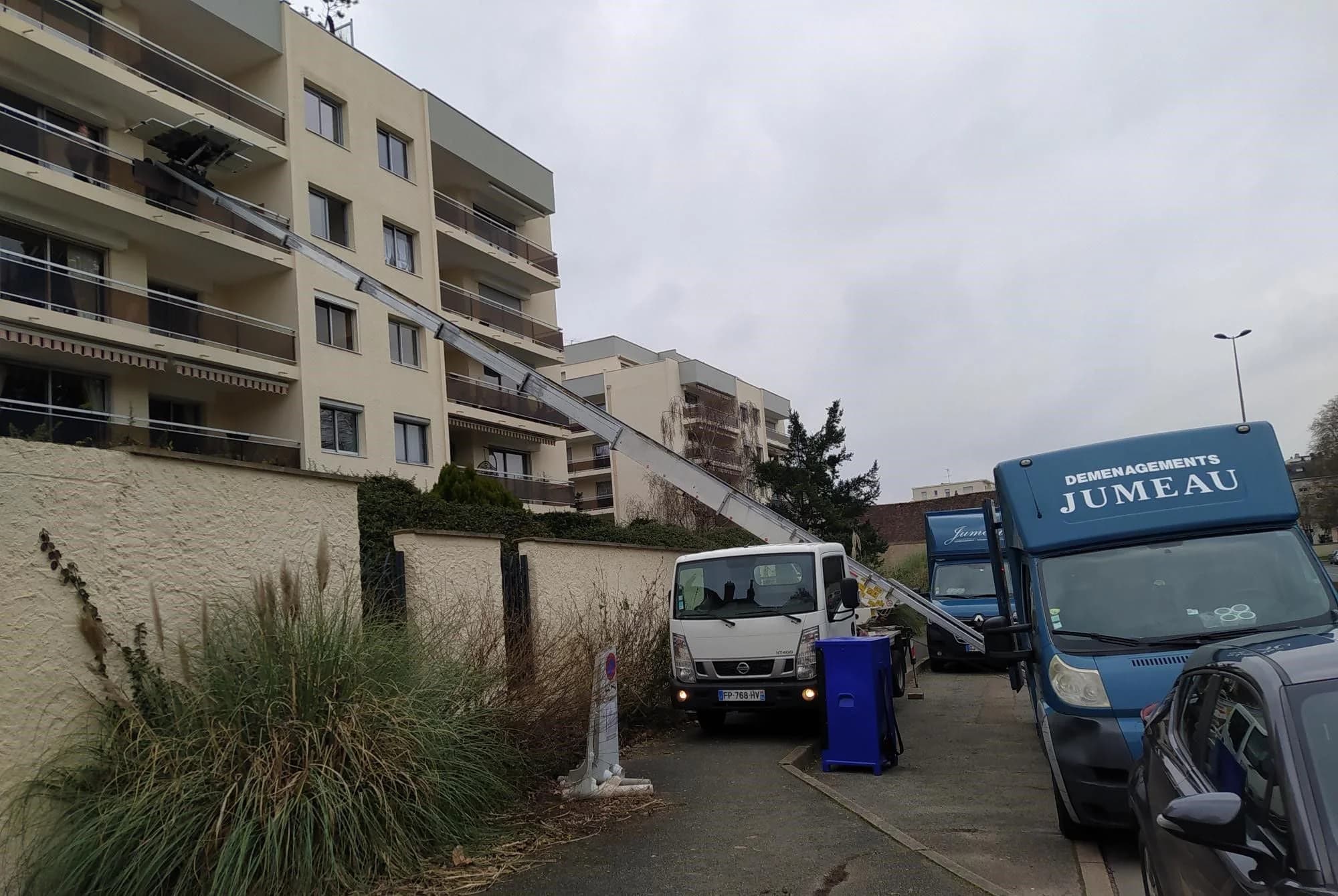 Un monte-meubles dressé contre la façade d’une résidence, à côté d’un camion des Déménagements Jumeau