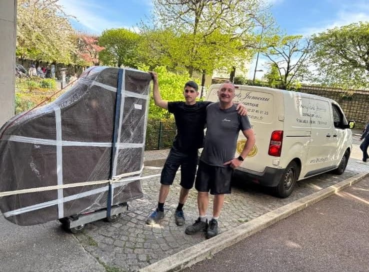 Deux déménageurs à côté d’un piano emballé sur son chariot, devant un fourgon Jumeau, à Paris