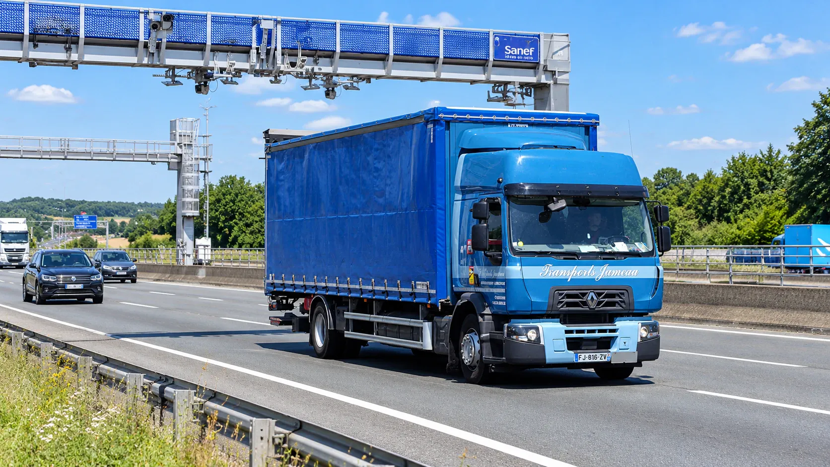 Un porteur bâché bleu des Transports Jumeau passe sous un portique d’autoroute